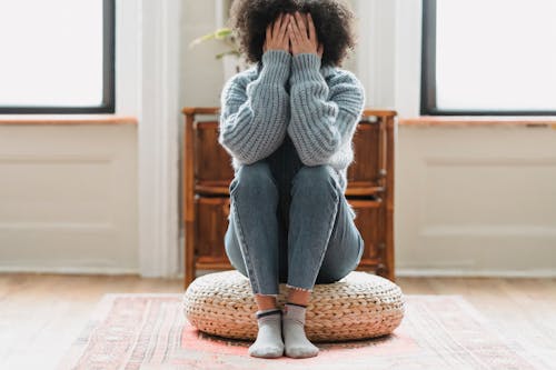 Free Full body of anonymous depressed female in casual clothes sitting on rattan stool in light room with windows at home Stock Photo