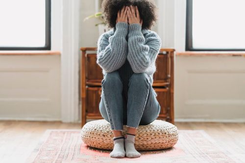 Free Full body of anonymous depressed female in casual clothes sitting on rattan stool in light room with windows at home Stock Photo