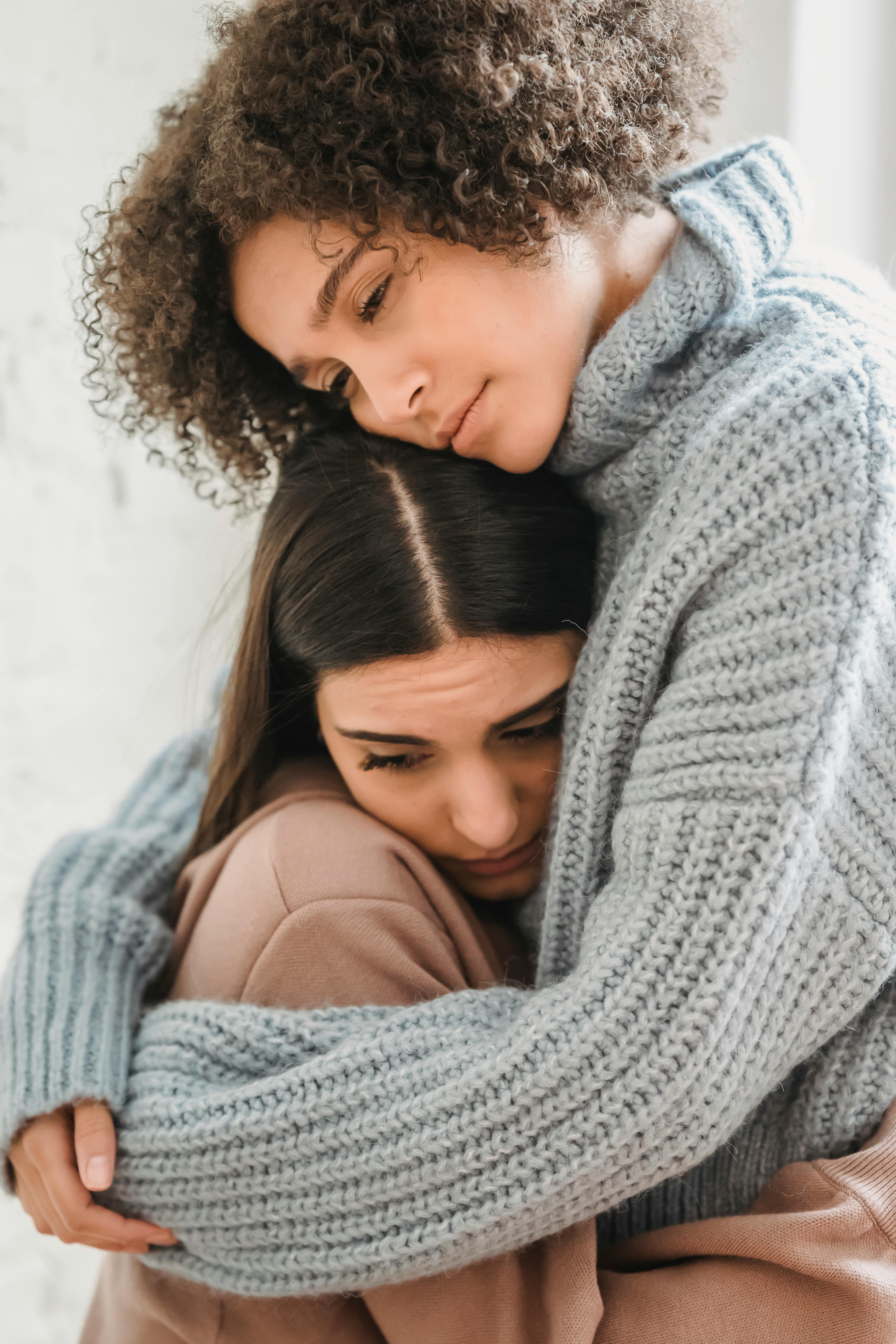 sad multiethnic women hugging in room