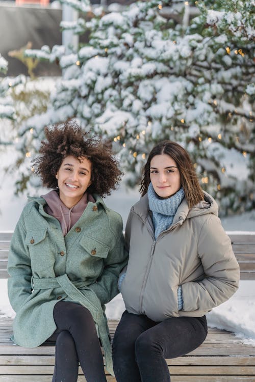 Smiling diverse women sitting on on bench in winter day