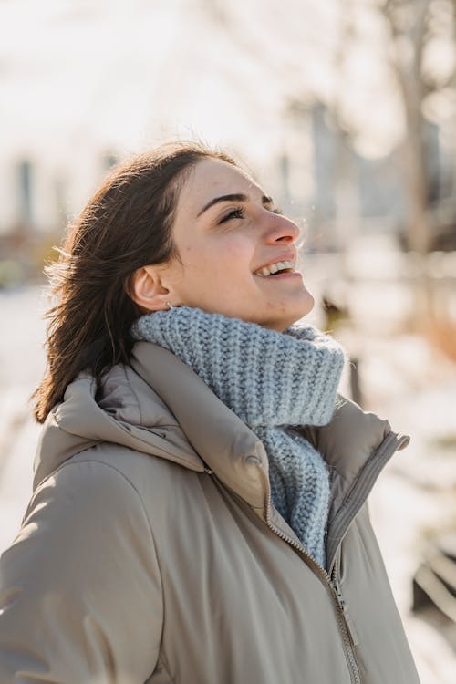 Side view of smiling female in warm clothes standing on street in city on blurred background on cold winter day