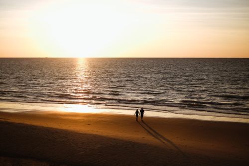 Free Silhouetted couple walking on Miri Beach, Sarawak at sunset, reflecting romantic tranquility. Stock Photo