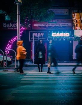 Blurred night scene showcasing pedestrians on a neon-lit street crosswalk, embodying urban energy.