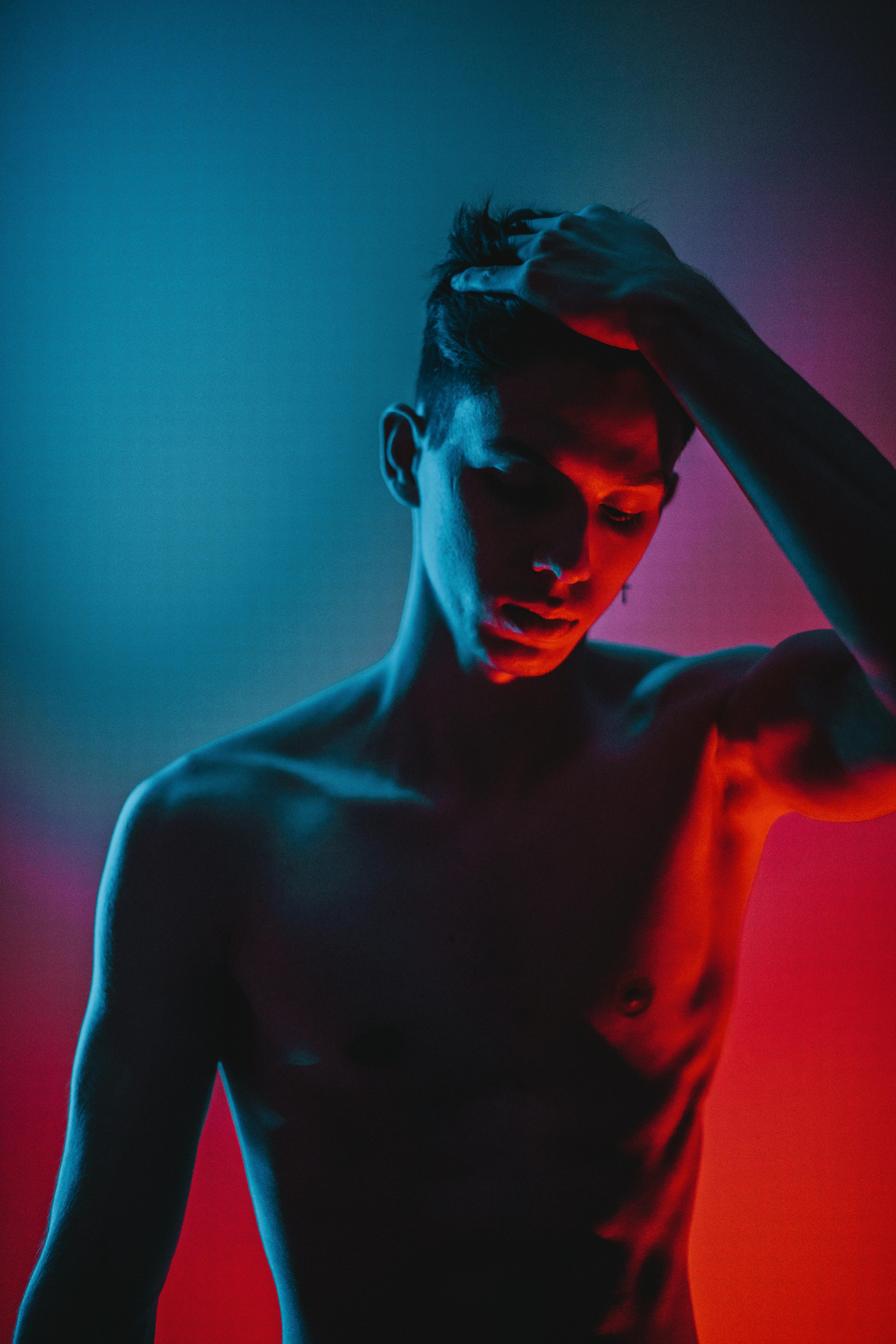 fit shirtless man touching hair and standing in neon lights