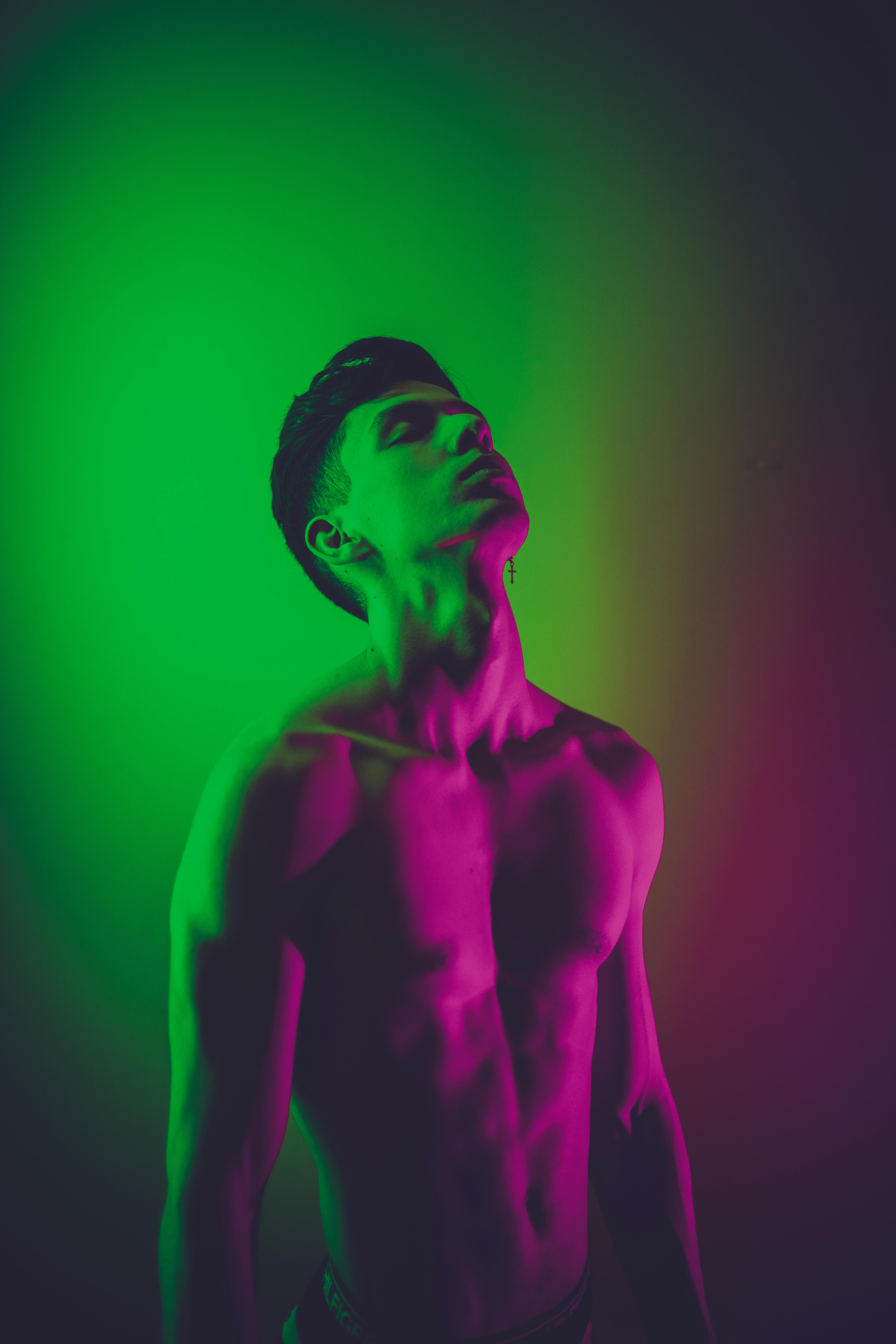 fit shirtless man standing with eyes closed in neon lights