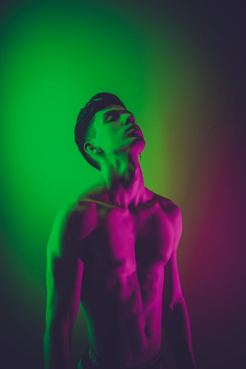 Fit shirtless man standing with eyes closed in neon lights