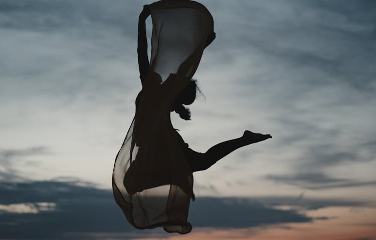 Silhouette Of A Woman Jumping On Air Holding A Scarf