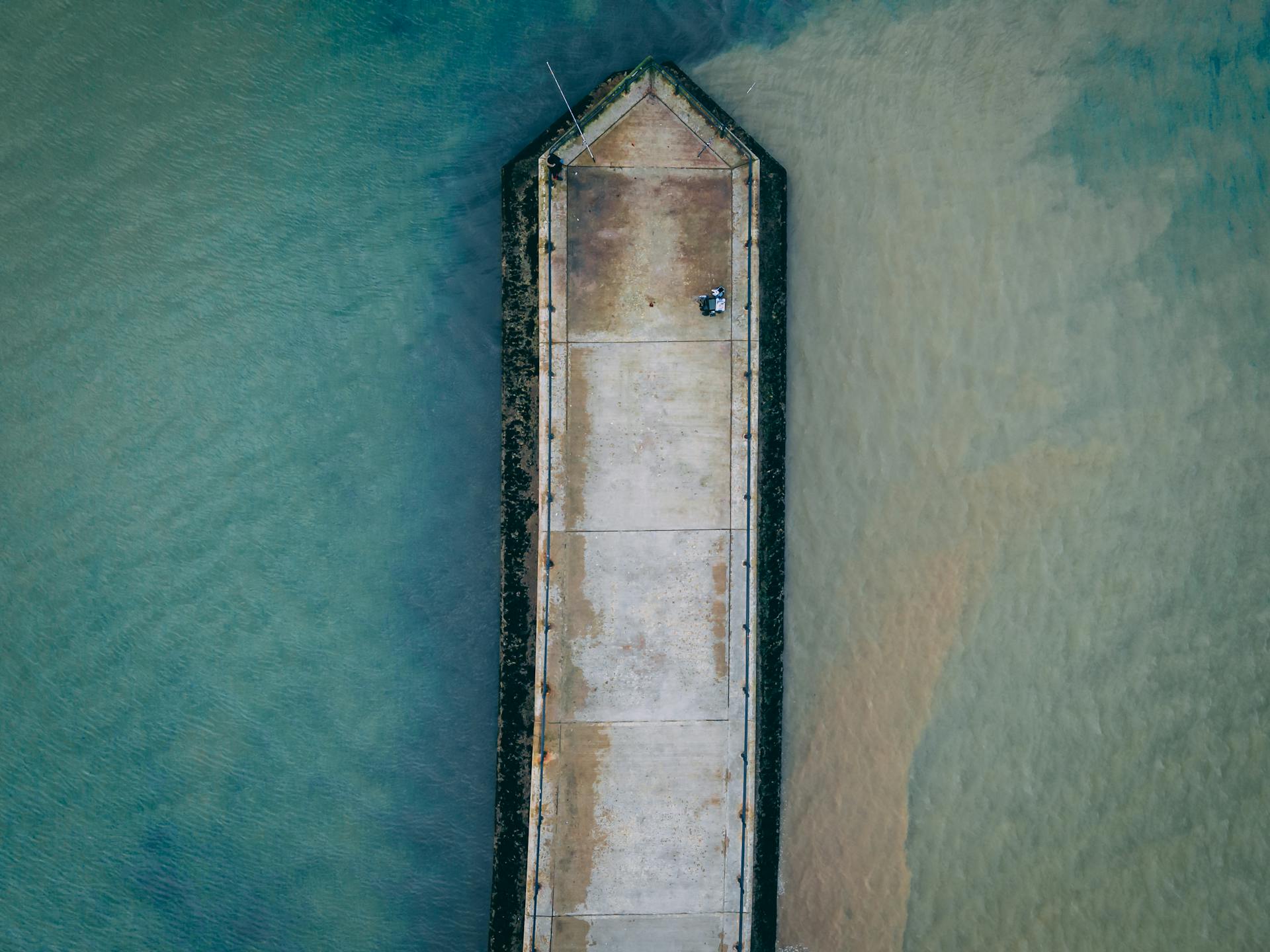 Drone shot of a concrete dock extending into calm waters in England.