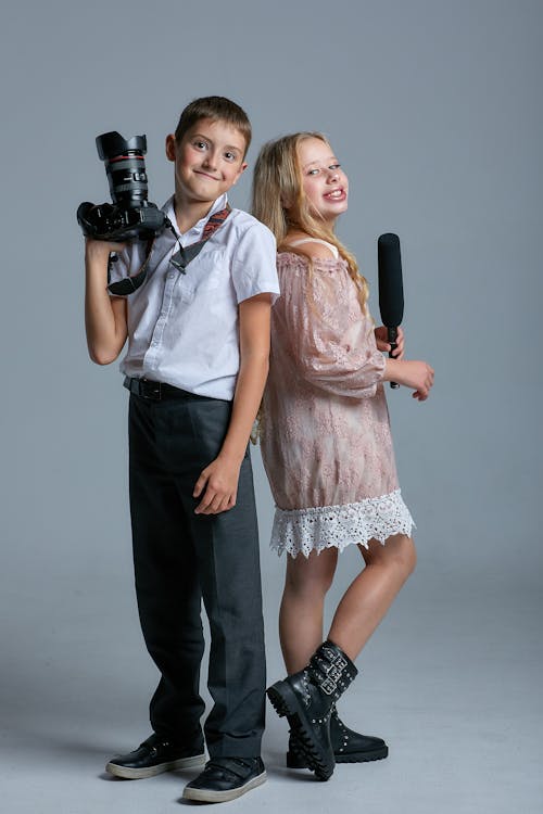 Free A Boy Holding a Camera Beside a Girl Holding Microphone Stock Photo