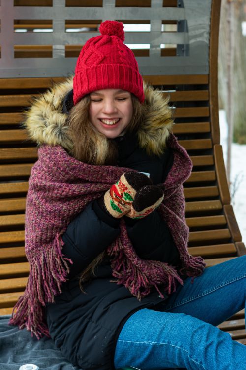 Free Smiling woman in winter attire sitting outdoors, enjoying the cold weather. Stock Photo