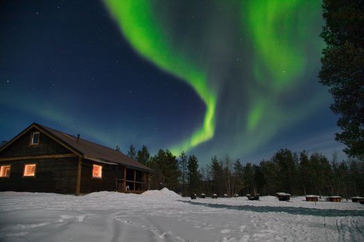 Enchanting northern lights over a snowy cabin in Kiruna, Sweden.
