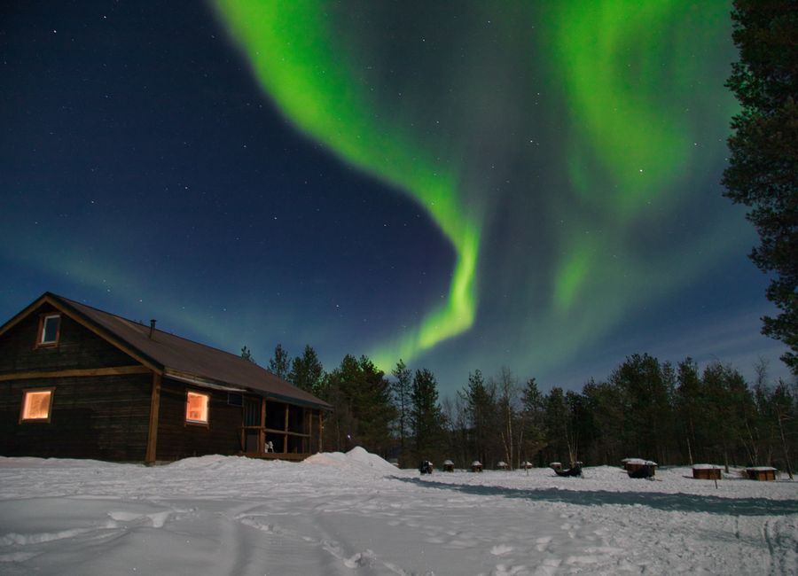 Enchanting northern lights over a snowy cabin in Kiruna, Sweden.