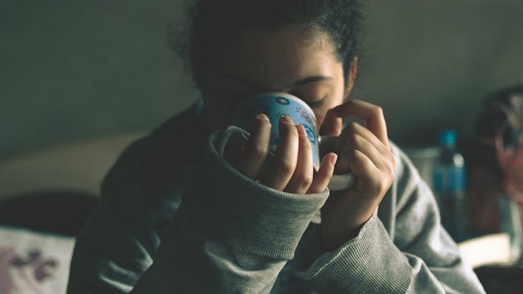 Crop Calm Woman Drinking Hot Beverage On Bed