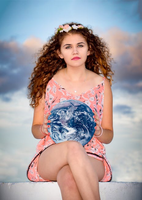 Woman Wearing Pink Floral Sleeveless Romper Sitting on Gray Concrete Holding Earth Globe