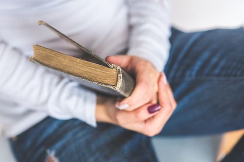 Free A woman gently holding an old book, showcasing a close-up view indoors with a focus on the hands and the book. Stock Photo