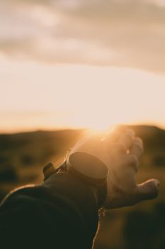 Silhouette of a hand reaching towards the warm sunset light, capturing a serene moment outdoors.