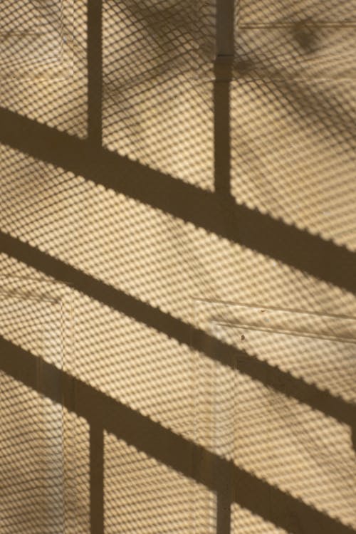Abstract background of beige concrete building wall with net fence shadows in daylight