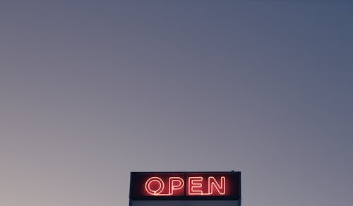 From below of illuminated signboard with Open red neon inscription against cloudless sunset sky