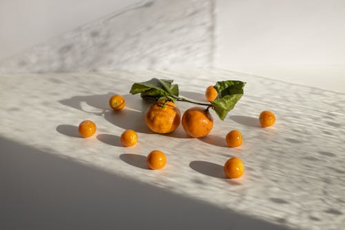 Healthy tangerines and groundcherries scattered on white surface in daylight