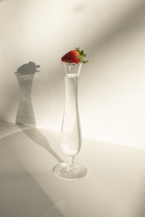 From above of fresh ripe strawberry on elegant crystal glass with transparent alcohol drink  against white background in sunlight