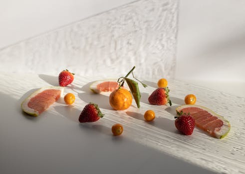 From above of fresh ripe strawberries and groundcherries scattered on white table with whole unpeeled tangerine and grapefruit slices