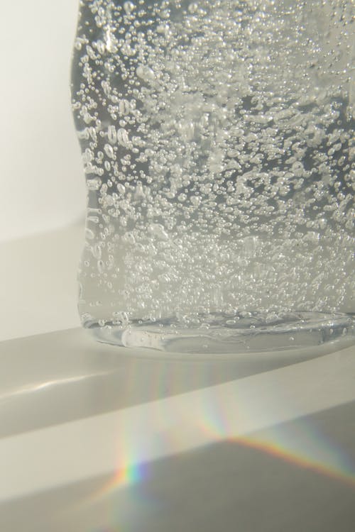 Clear cold sparkling water with bubbles in transparent glass vase placed on white table in sunlight
