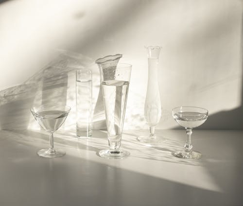 From above set of classic crystal glasses of various shapes with water served on white table in sunlight