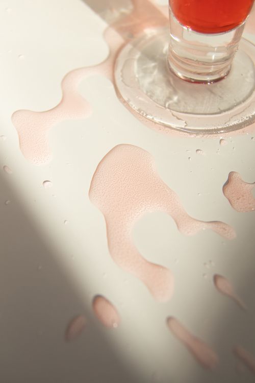 Free From above glass of red colored beverage spilled on white table in sunlight Stock Photo