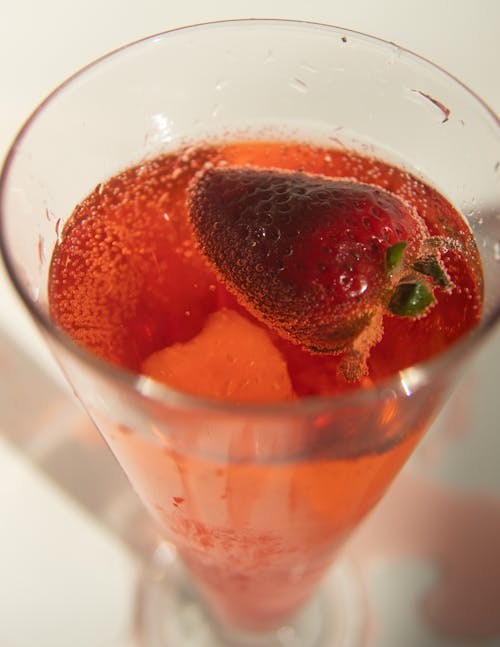 High angle of glass of refreshing fizzy soda drink with strawberry served on white table