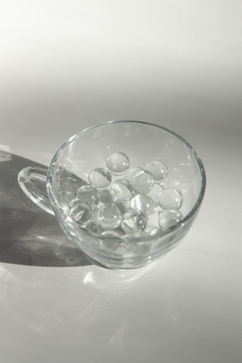 Glass cup with small transparent balls on white surface