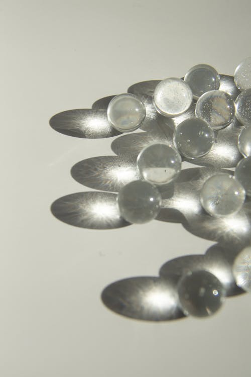 High angle of heap of small transparent glass balls scattered on white surface and shading in sunlight