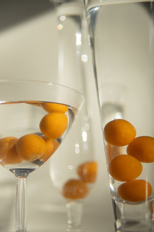 From above of cocktails in various glasses decorated with yellow fresh Physalis fruits against white background in sunlight
