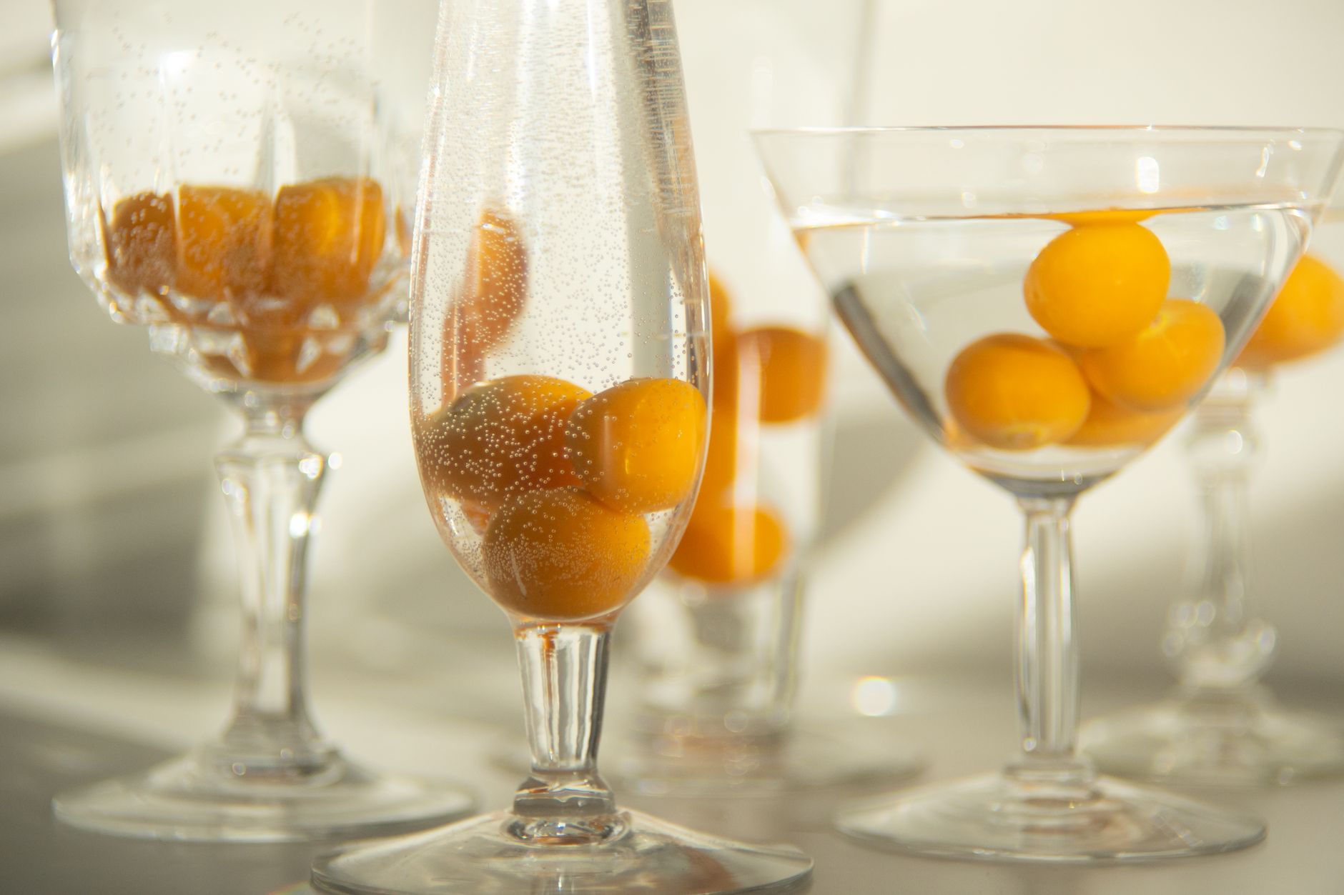 Bright ripe cumquats in assorted glasses with pure water in sunlight on white background