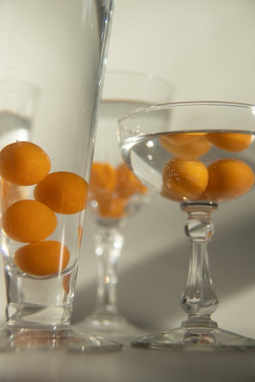 Whole ripe cumquats in glassware with pure aqua with shiny surface on white background