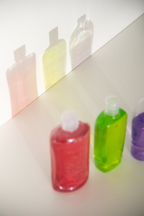 Free From above of assorted plastic bottles with colorful gels in row reflecting on white wall Stock Photo