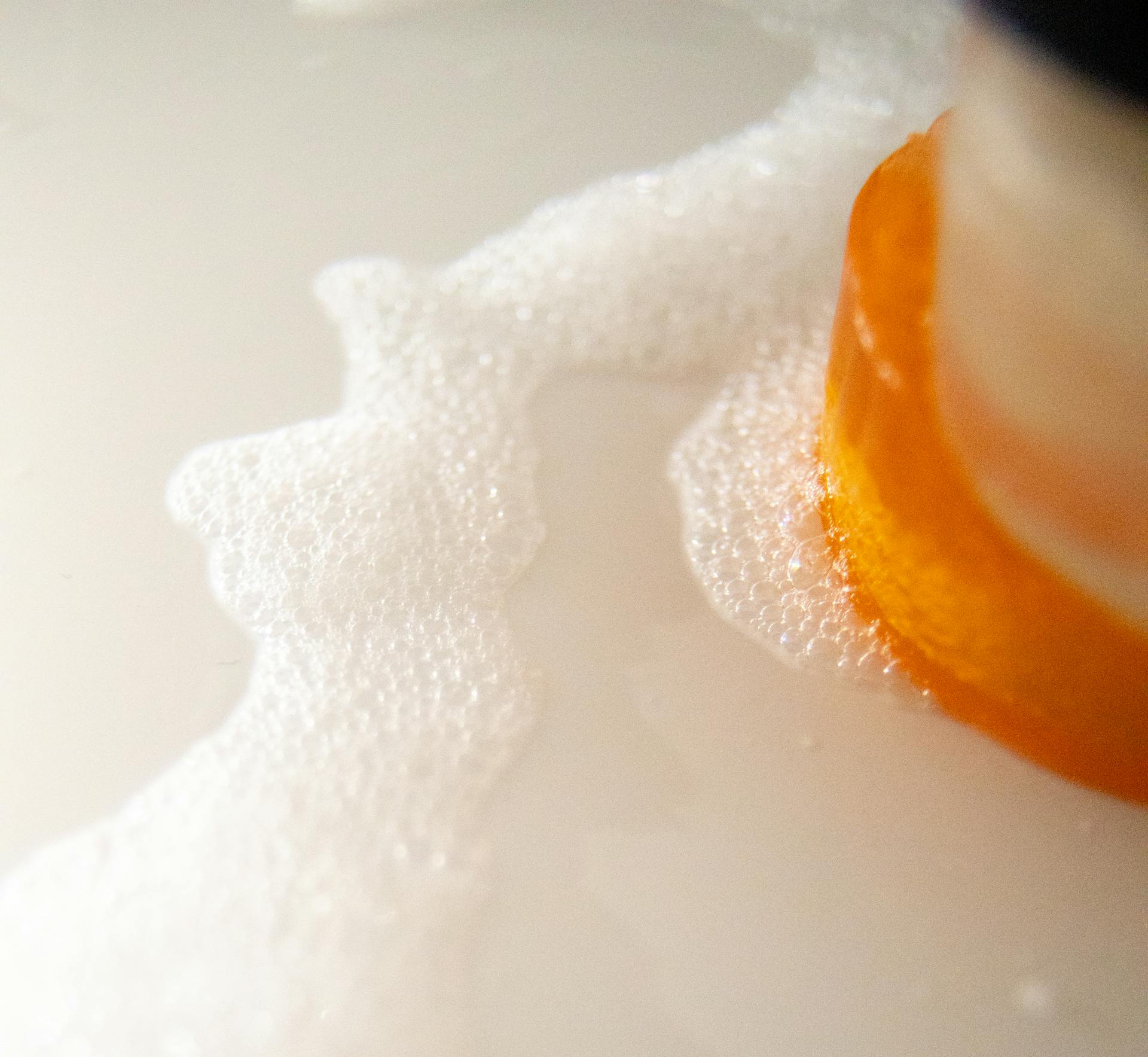 High angle of pile of colorful soaps near foam flow with small bubbles on white surface