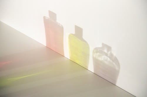 From above of different bottle shadows with bright liquids and caps in row on smooth surface