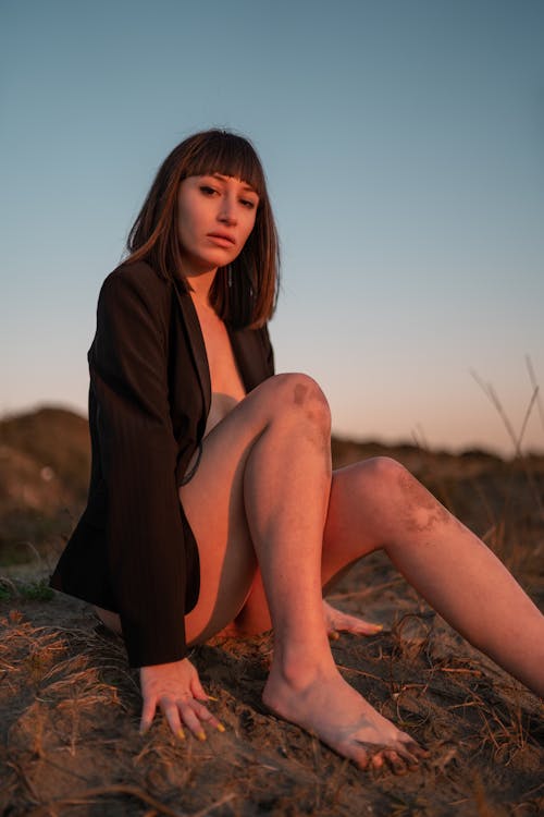 Barefooted Woman Sitting on the Dirt Ground Wearing Only a Jacket