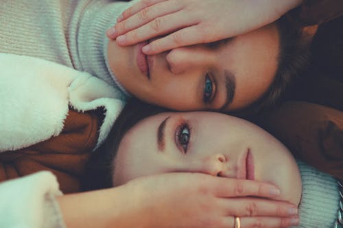 Free Top view of best female friends covering eye to each other while lying and looking at camera Stock Photo
