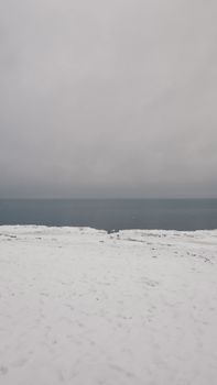 Scenery view of snowy coast against endless ocean with horizon line under gray sky in winter