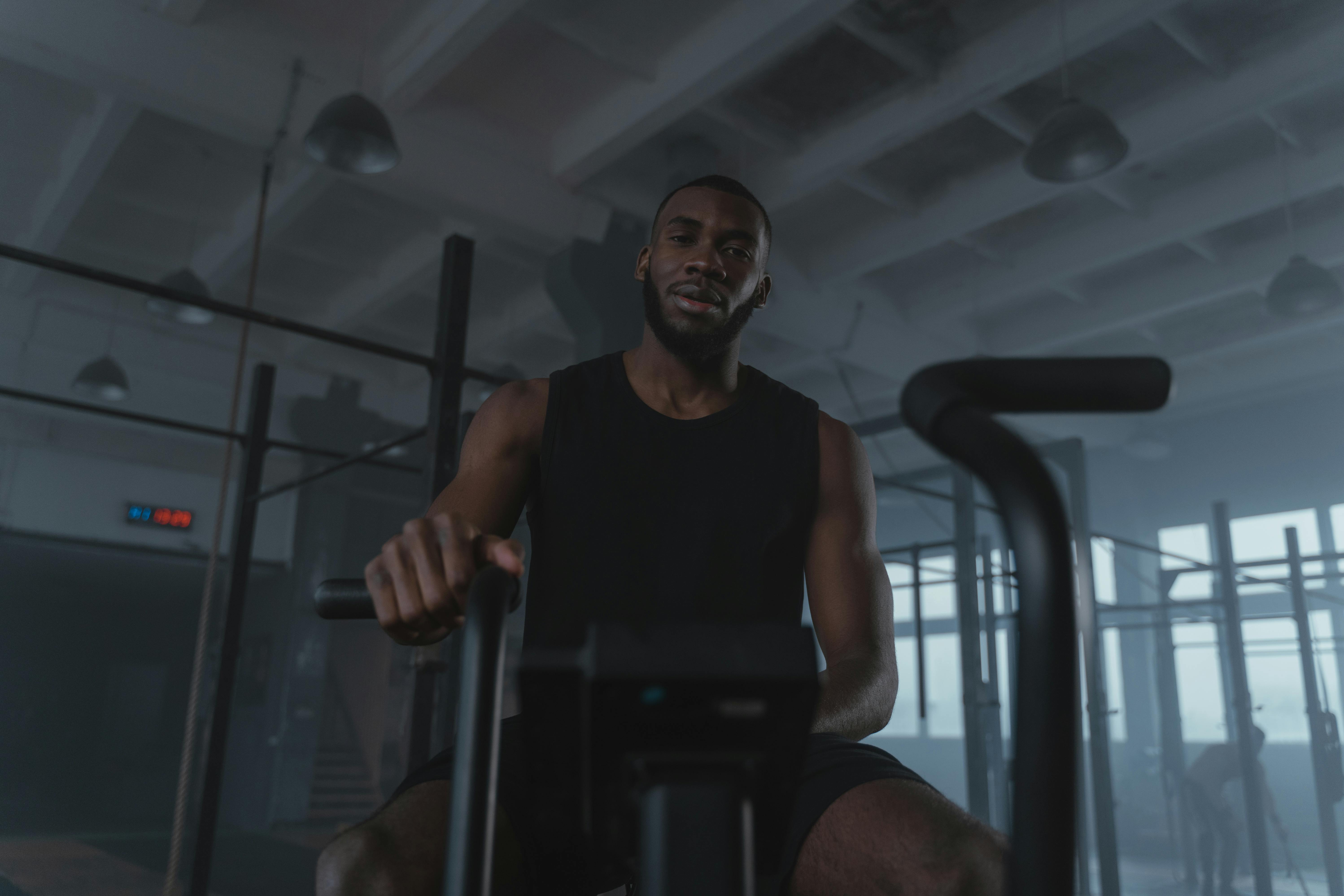 Black man training on exercise bike in modern gym setting, promoting fitness and healthy lifestyle.