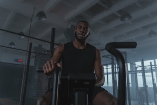 Black man training on exercise bike in modern gym setting, promoting fitness and healthy lifestyle.