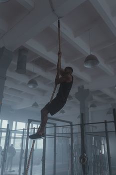 Man climbing a rope in a gym, showcasing strength and fitness in a modern indoor setting.