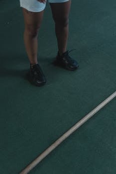 Closer view of legs in sneakers on a green carpeted floor, with a stick in frame.