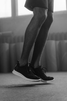 Grayscale image of legs in motion, wearing sneakers, inside a gym setting.