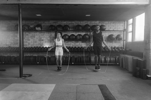 Two athletes jump rope in an industrial-style gym with brick walls and equipment.