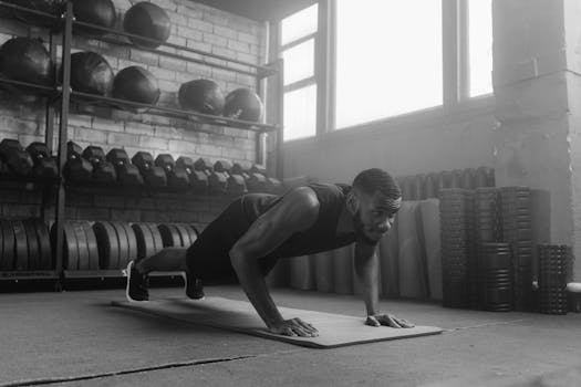 Monochrome image of a man doing push-ups on a mat in a gym setting.