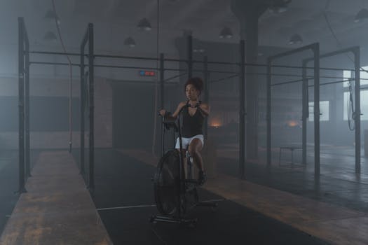 A woman works out on a stationary bike in a dimly lit gym setting, promoting fitness and healthy living.