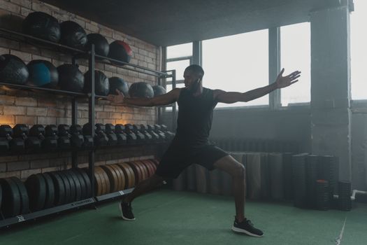 A muscular black man stretching in a modern gym with fitness equipment, promoting healthy living.