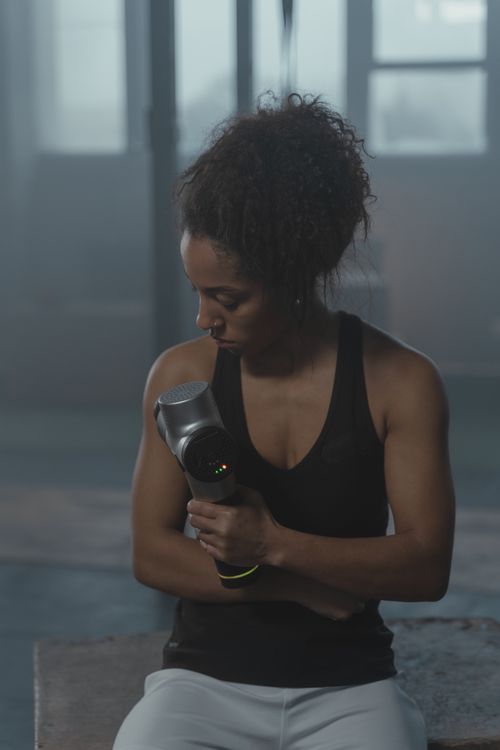 Free Fit woman using a massage gun in a gym for muscle recovery. Stock Photo